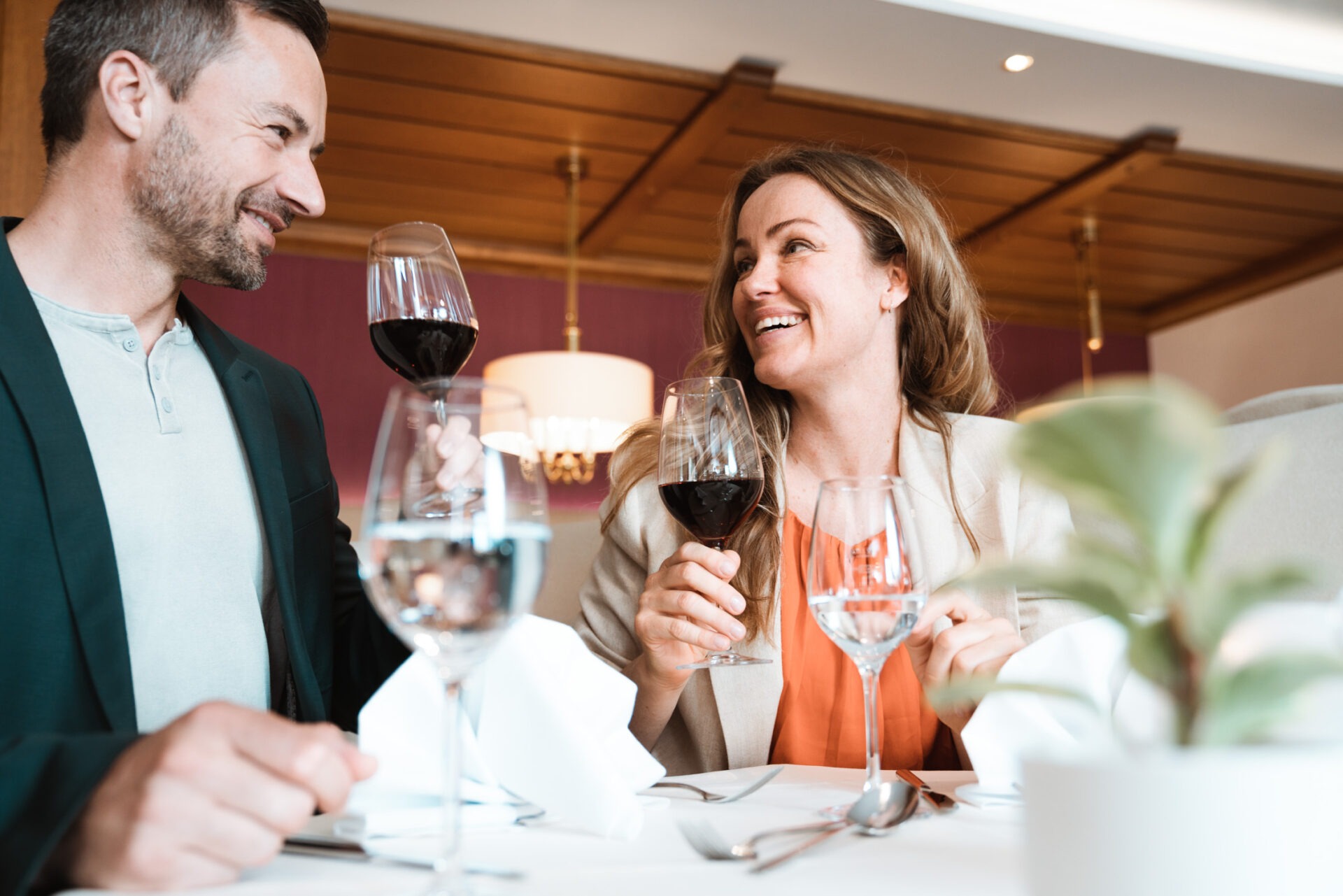 zwei Gäste die sich anlächeln und dabei ein Rotweinglas in der Hand halten und anstoßen